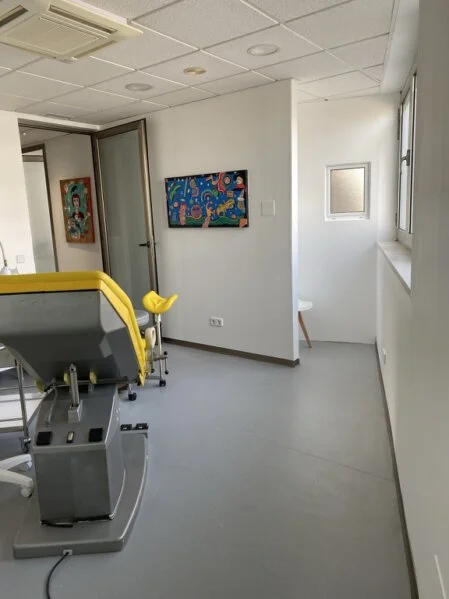 Behandlungsstuhl mit Kunstwerk von Arthur Brauner im hellen Untersuchungsraum.